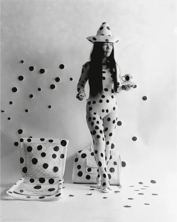 Black and white photograph of a young Yayoi Kusama in a performance with dots